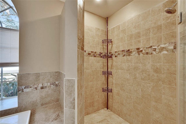 bathroom featuring a healthy amount of sunlight, tile walls, and tiled shower