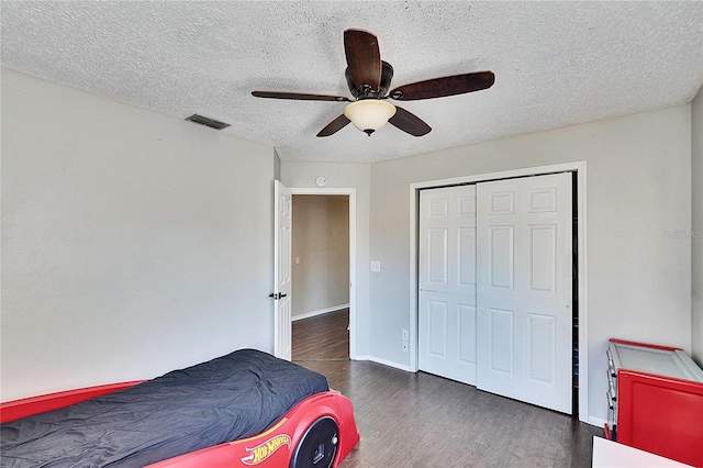 bedroom featuring dark wood-type flooring, a textured ceiling, ceiling fan, and a closet