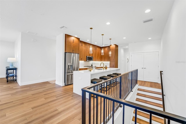 kitchen featuring sink, a breakfast bar area, appliances with stainless steel finishes, a center island with sink, and decorative light fixtures