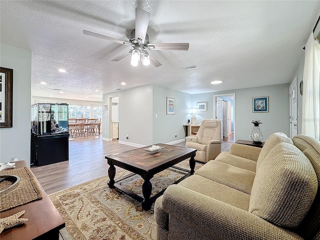 living room with ceiling fan, a textured ceiling, and light wood-type flooring