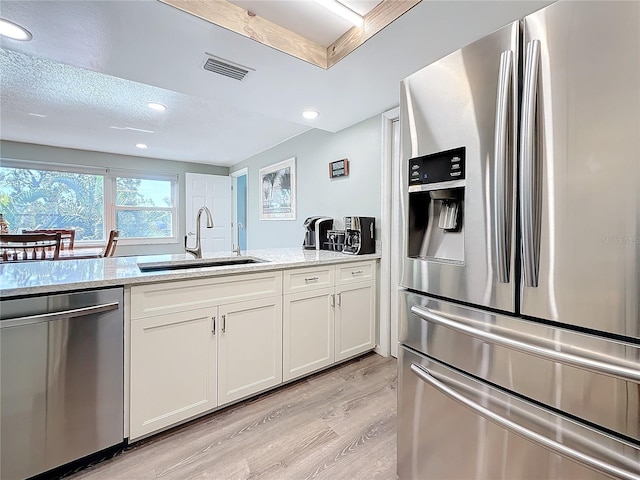 kitchen with sink, light stone counters, appliances with stainless steel finishes, light hardwood / wood-style floors, and white cabinets