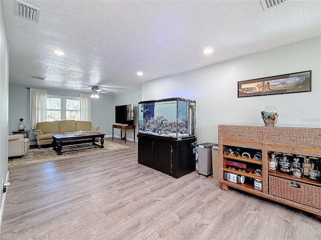 living room featuring ceiling fan, a textured ceiling, and light wood-type flooring