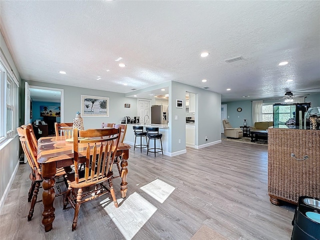 dining area with ceiling fan, light hardwood / wood-style flooring, and a textured ceiling