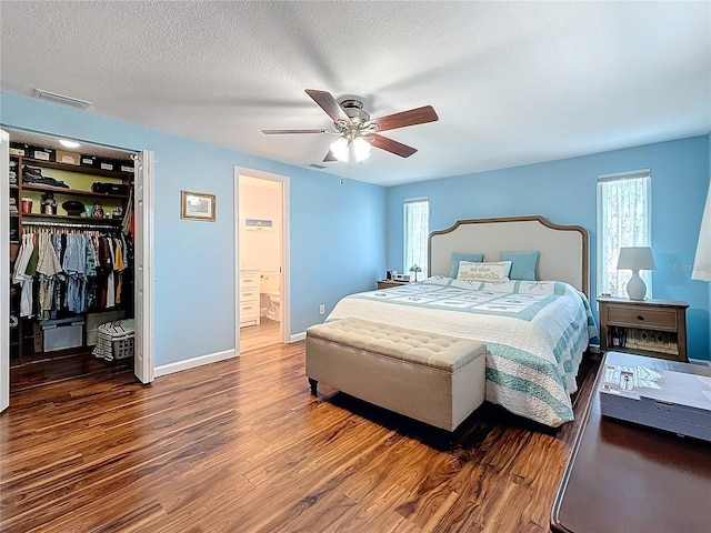 bedroom with a walk in closet, a textured ceiling, dark hardwood / wood-style flooring, a closet, and ceiling fan