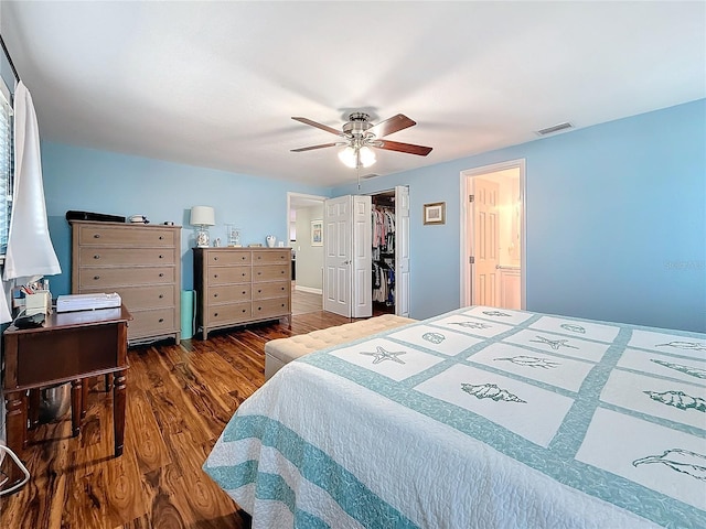 bedroom with a walk in closet, dark wood-type flooring, and ceiling fan