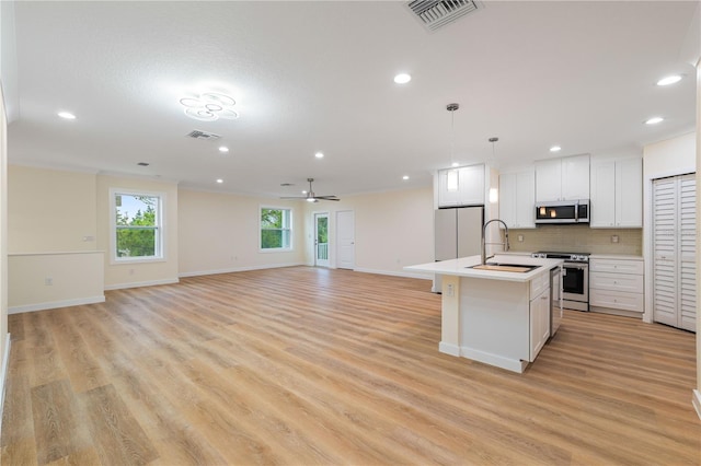 kitchen featuring appliances with stainless steel finishes, decorative light fixtures, an island with sink, white cabinets, and decorative backsplash