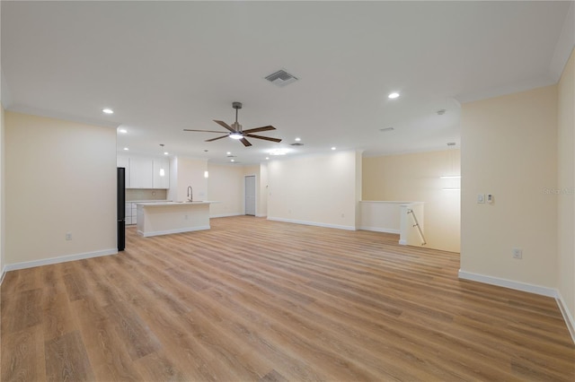 unfurnished living room featuring ceiling fan, ornamental molding, sink, and light wood-type flooring