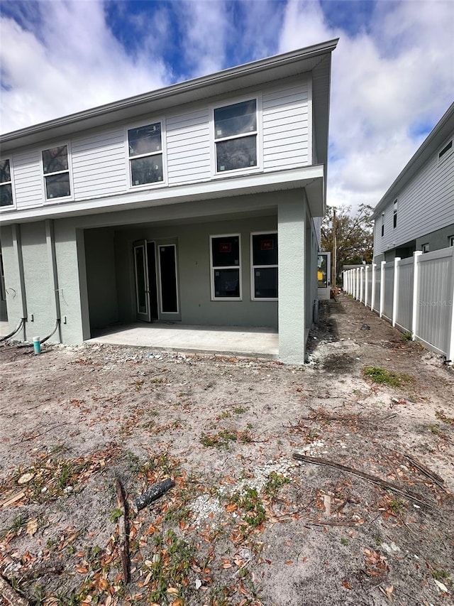 rear view of house featuring a patio area, fence, and stucco siding