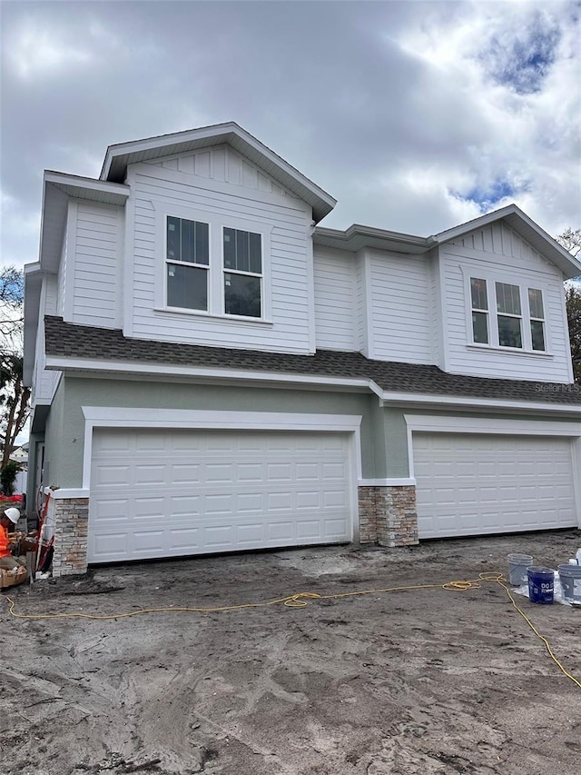 view of front of home with stone siding, roof with shingles, and an attached garage