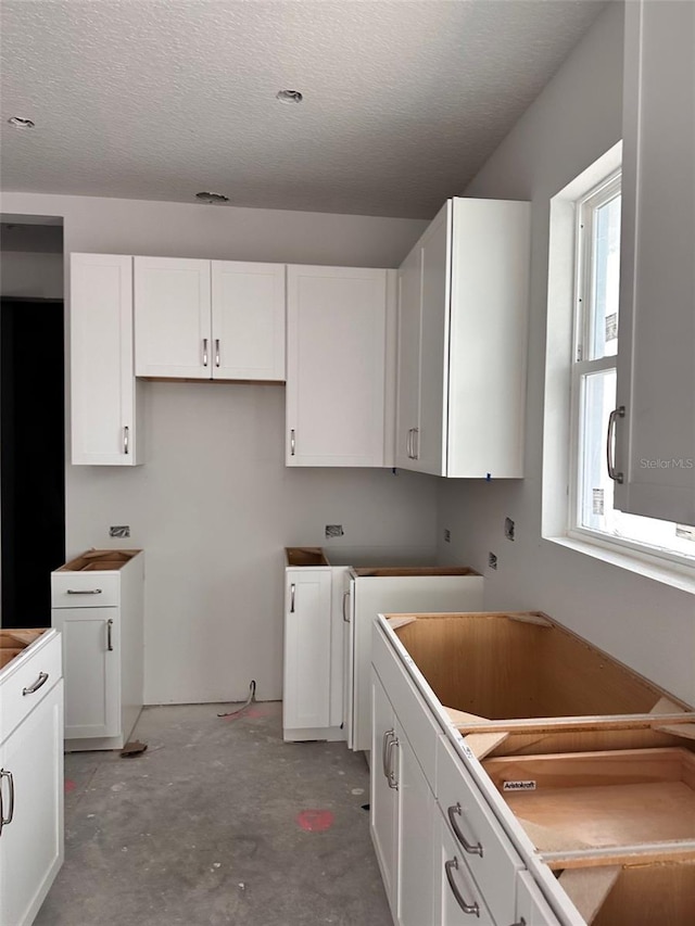 kitchen featuring concrete flooring, white cabinetry, and a textured ceiling