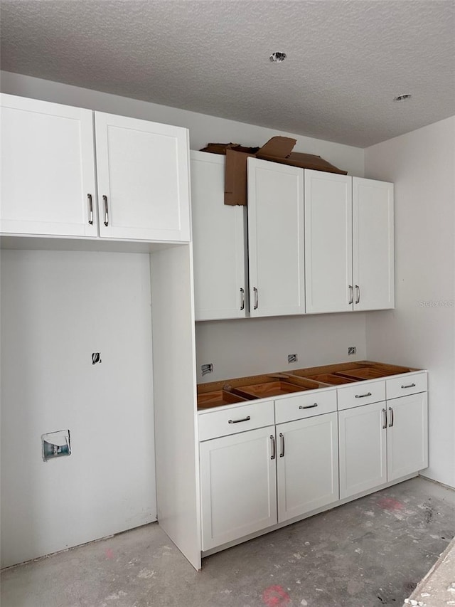 kitchen featuring a textured ceiling, concrete floors, and white cabinetry