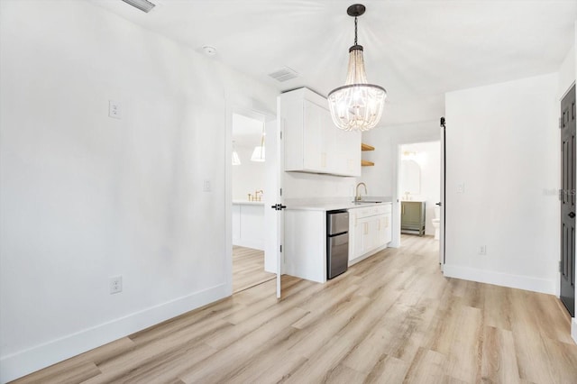 kitchen with sink, white cabinetry, a notable chandelier, decorative light fixtures, and light wood-type flooring