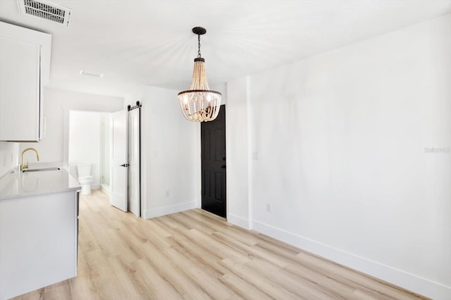 unfurnished dining area featuring sink, a chandelier, and light wood-type flooring