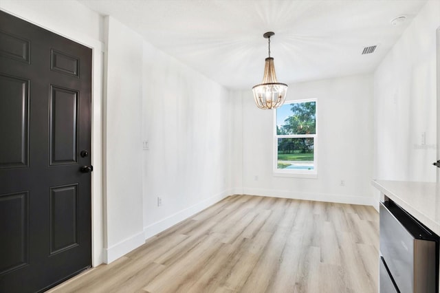 unfurnished dining area with an inviting chandelier and light wood-type flooring