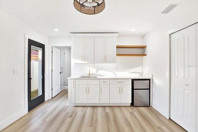 kitchen with white cabinetry, sink, light hardwood / wood-style floors, and stainless steel refrigerator