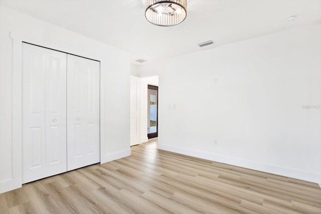 unfurnished bedroom featuring a chandelier, light hardwood / wood-style floors, and a closet