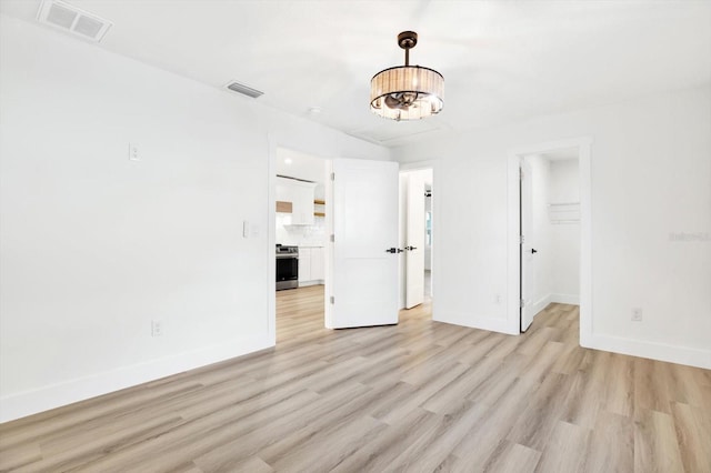 unfurnished room featuring a notable chandelier and light wood-type flooring