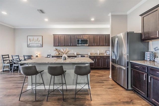 kitchen with stainless steel appliances, dark brown cabinets, a kitchen island with sink, and a breakfast bar area