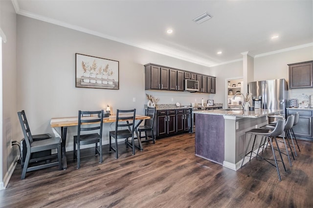 kitchen with a kitchen bar, dark brown cabinets, a center island with sink, and appliances with stainless steel finishes