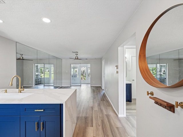 kitchen with sink, light stone counters, a textured ceiling, light wood-type flooring, and ceiling fan