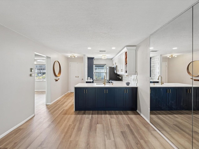 kitchen with tasteful backsplash, white cabinetry, stainless steel fridge, light hardwood / wood-style floors, and kitchen peninsula