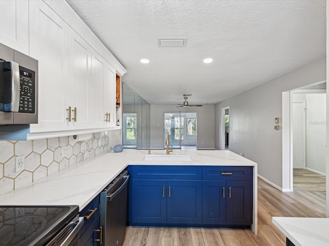 kitchen with blue cabinetry, sink, white cabinetry, kitchen peninsula, and stainless steel appliances