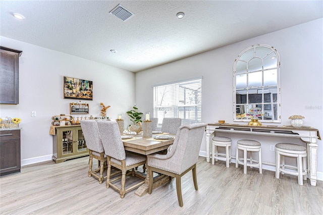 dining space with a textured ceiling and light hardwood / wood-style flooring