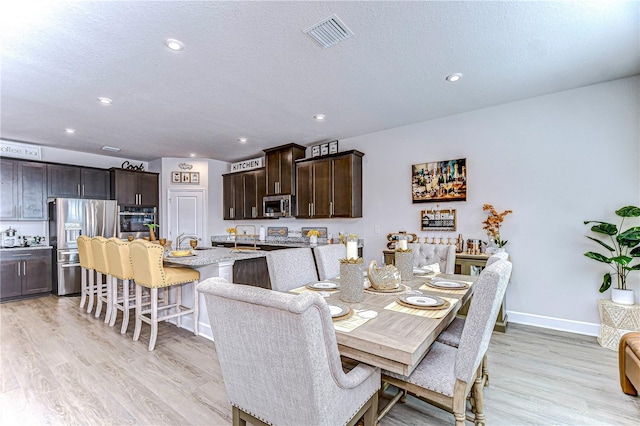 dining room featuring sink, a textured ceiling, and light wood-type flooring