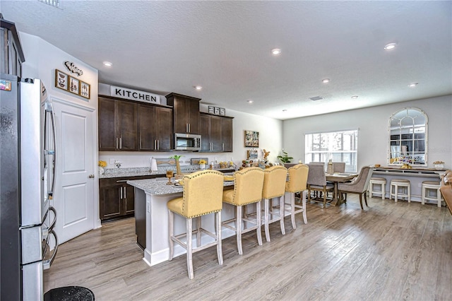 kitchen with dark brown cabinetry, a breakfast bar area, a center island, light hardwood / wood-style flooring, and stainless steel appliances