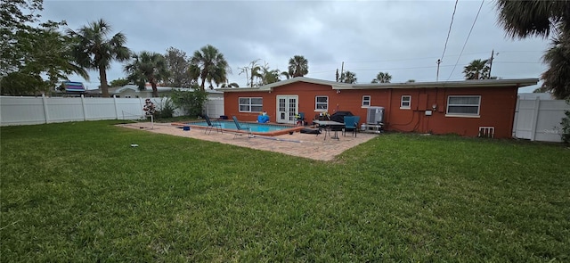 rear view of house with a fenced in pool, a lawn, and a patio area