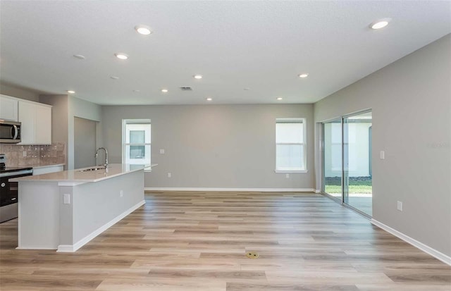 kitchen with appliances with stainless steel finishes, white cabinetry, backsplash, light hardwood / wood-style floors, and a center island with sink