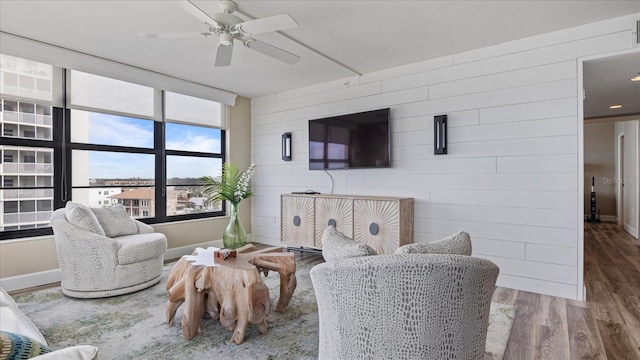 living room featuring wood-type flooring, wooden walls, and ceiling fan