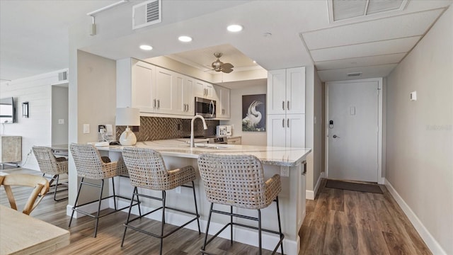 kitchen featuring light stone counters, dark hardwood / wood-style flooring, kitchen peninsula, ceiling fan, and white cabinets