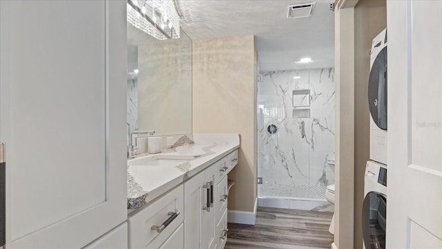 bathroom with toilet, wood-type flooring, a tile shower, vanity, and stacked washer / dryer