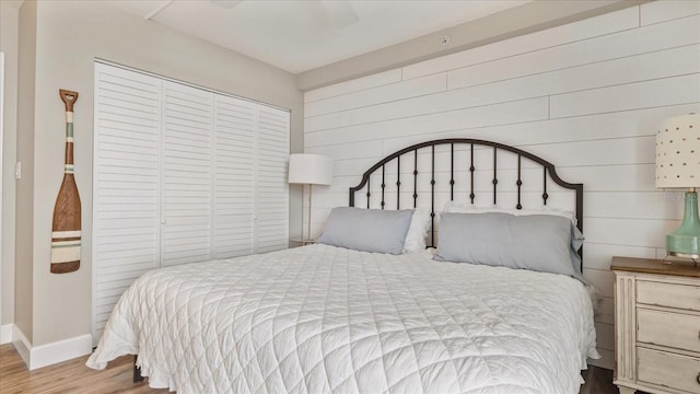 bedroom with wooden walls, wood-type flooring, a closet, and ceiling fan