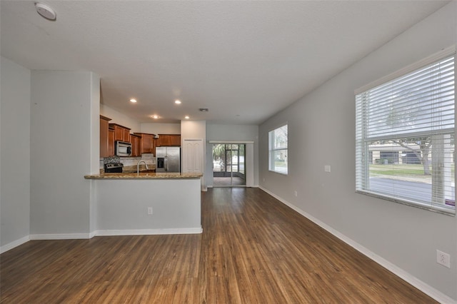 kitchen featuring appliances with stainless steel finishes, tasteful backsplash, sink, kitchen peninsula, and dark wood-type flooring