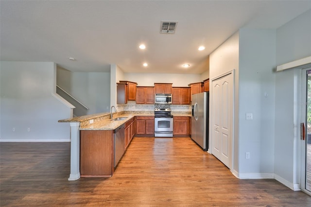 kitchen with sink, light stone counters, light wood-type flooring, kitchen peninsula, and stainless steel appliances