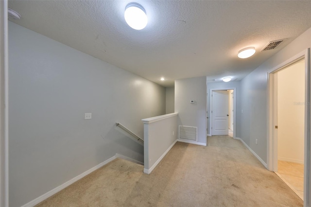 hall with light colored carpet and a textured ceiling