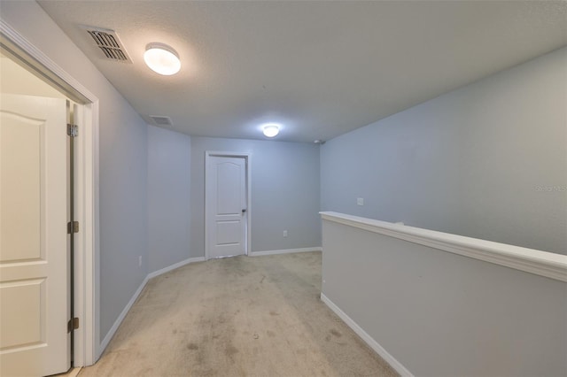 hall with light carpet and a textured ceiling