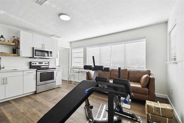 interior space with sink, white cabinetry, stainless steel appliances, a textured ceiling, and light wood-type flooring