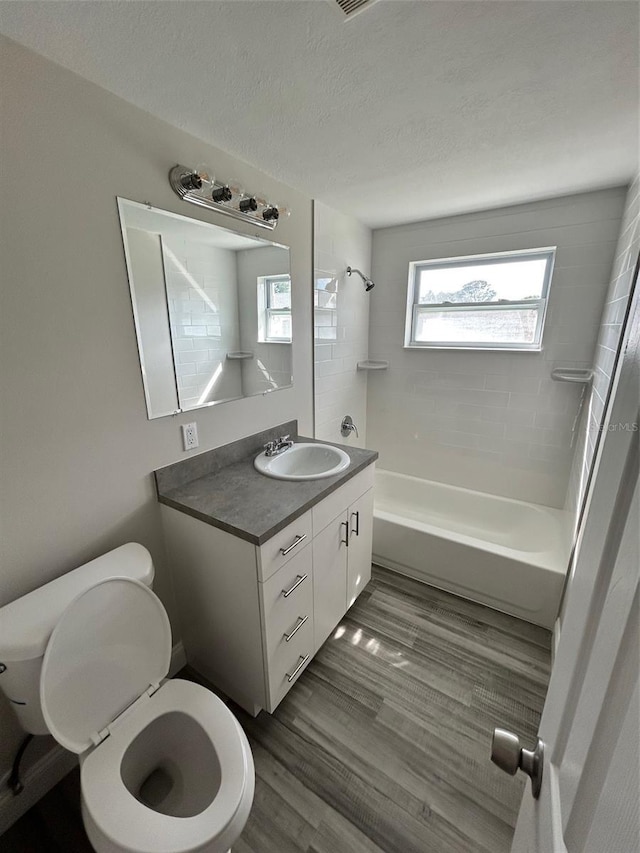 full bathroom featuring hardwood / wood-style flooring, vanity, tiled shower / bath combo, toilet, and a textured ceiling