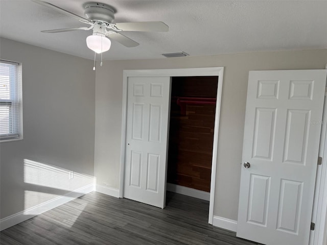 unfurnished bedroom featuring ceiling fan, a closet, a textured ceiling, and dark hardwood / wood-style floors