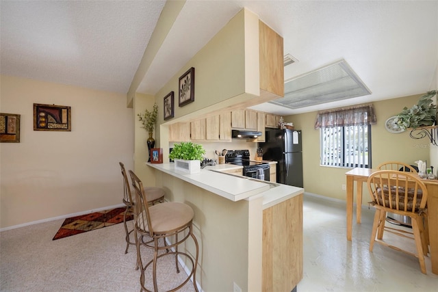 kitchen with a breakfast bar area, black appliances, a textured ceiling, kitchen peninsula, and light brown cabinets