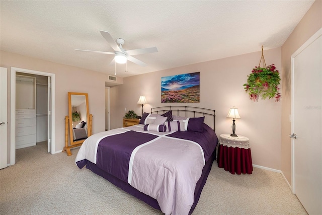 carpeted bedroom with a textured ceiling, a walk in closet, a closet, and ceiling fan