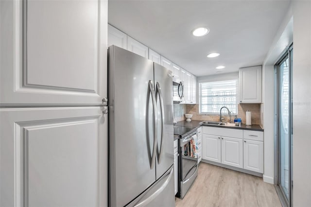 kitchen with tasteful backsplash, white cabinetry, sink, stainless steel appliances, and light wood-type flooring