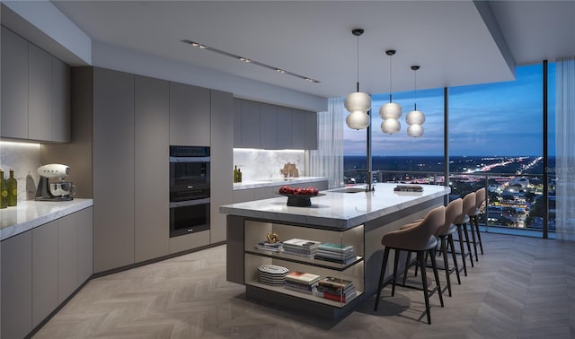 kitchen with pendant lighting, sink, gray cabinets, double oven, and a kitchen breakfast bar