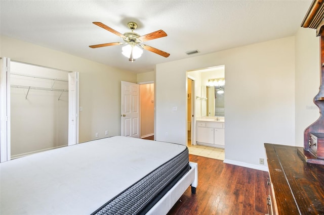 bedroom featuring ensuite bathroom, a wood stove, dark hardwood / wood-style flooring, a closet, and ceiling fan