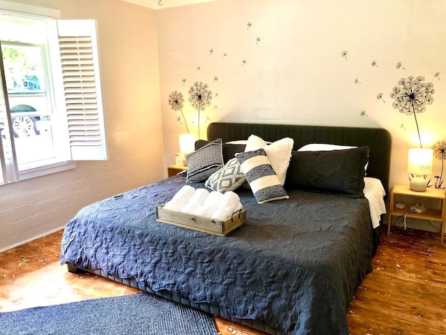 bedroom with multiple windows, brick wall, and dark hardwood / wood-style floors