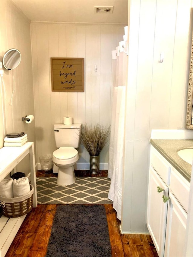 bathroom featuring hardwood / wood-style flooring, wooden walls, vanity, and toilet