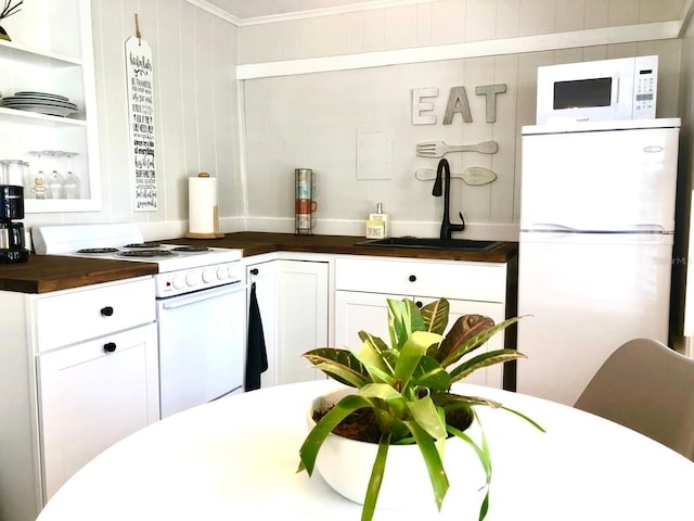 kitchen with wood walls, sink, white cabinets, ornamental molding, and white appliances